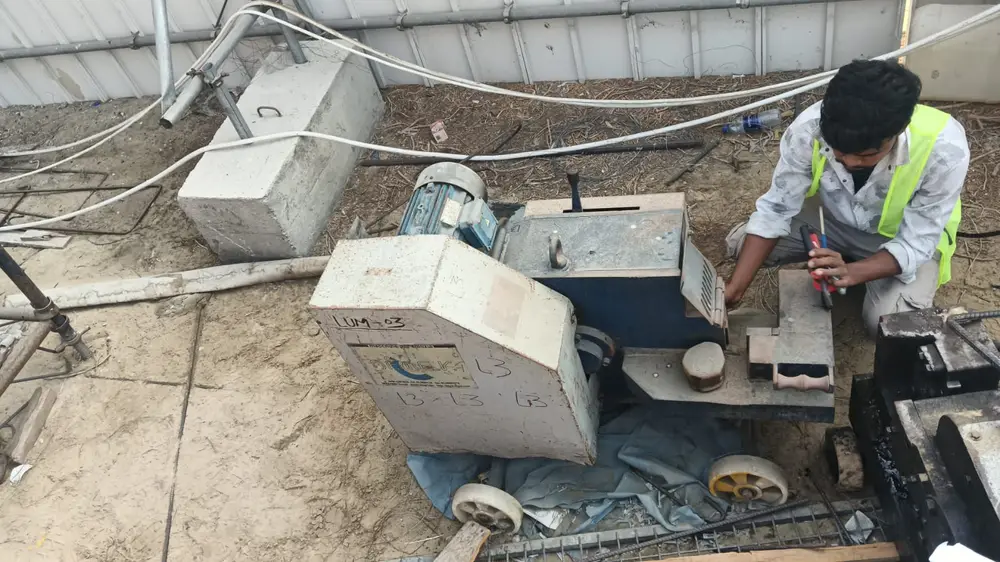 AMACO technician in hi-vis repairing a rebar cutting machine on site at a UAE construction site